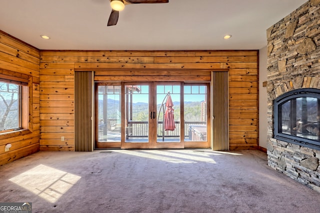 unfurnished living room featuring a stone fireplace, ceiling fan, carpet, and a healthy amount of sunlight