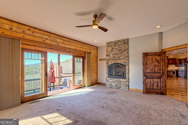 unfurnished living room with carpet flooring, ceiling fan, and a stone fireplace