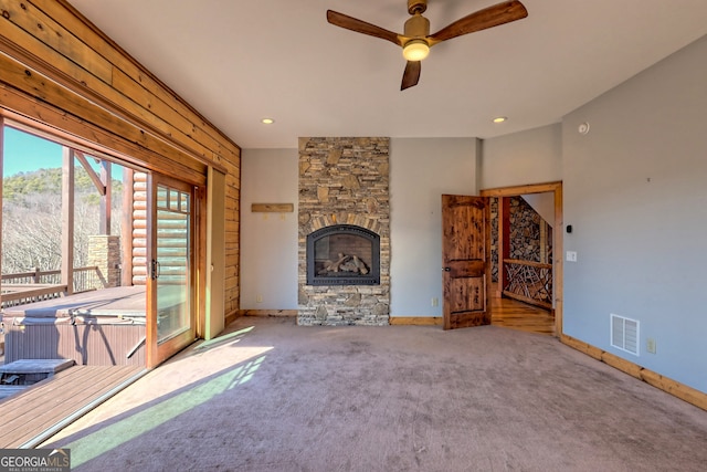 unfurnished living room featuring a stone fireplace, carpet, and ceiling fan