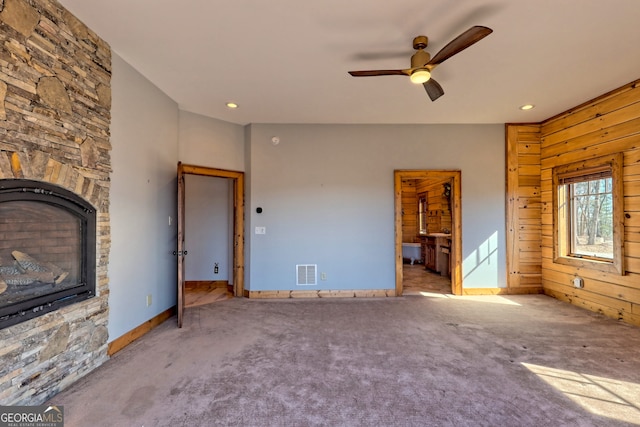 unfurnished living room with wood walls, ceiling fan, a fireplace, and carpet floors