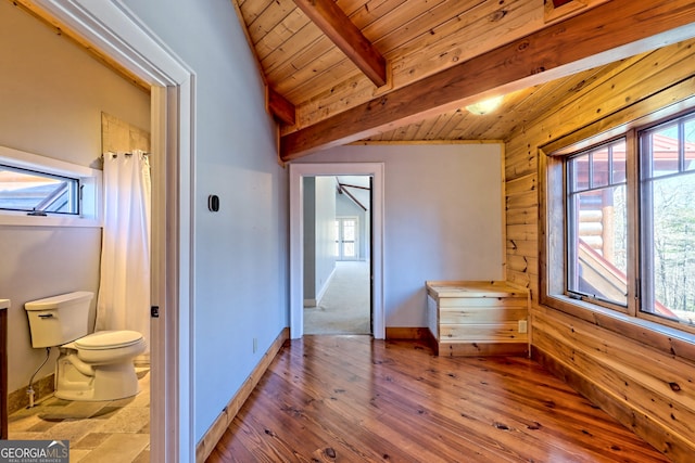 unfurnished bedroom featuring light hardwood / wood-style floors, ensuite bath, vaulted ceiling with beams, wood walls, and wooden ceiling