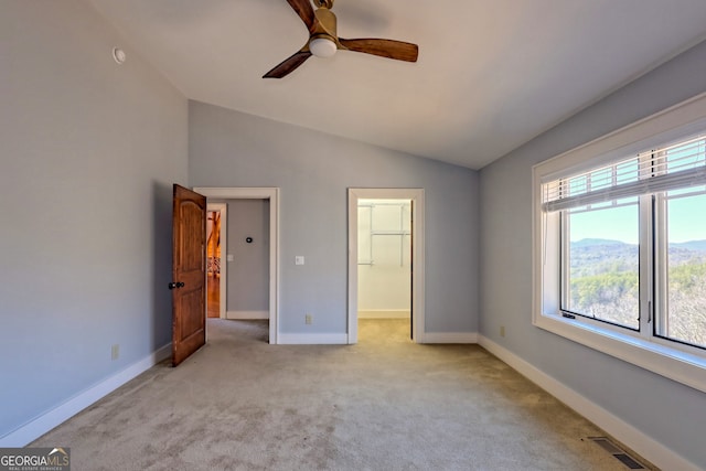 unfurnished bedroom with lofted ceiling, light carpet, ceiling fan, a closet, and a spacious closet