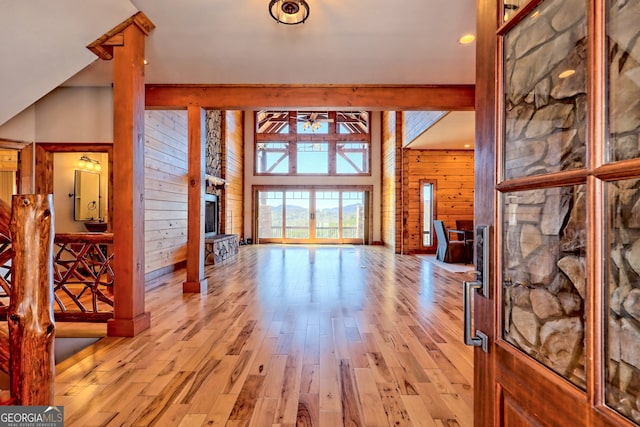 entryway with a fireplace, a towering ceiling, wood walls, and light hardwood / wood-style flooring