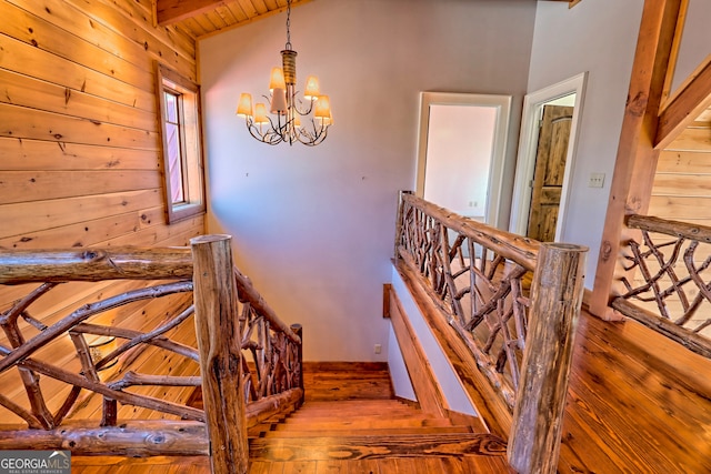 stairway featuring an inviting chandelier, wooden walls, wood-type flooring, and vaulted ceiling with beams