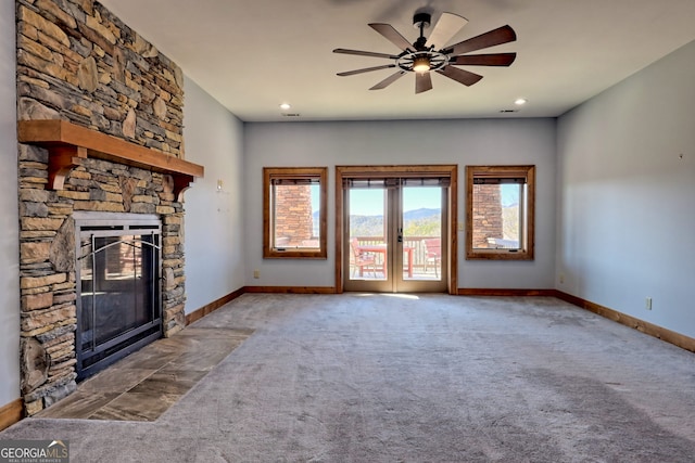 unfurnished living room with a stone fireplace, carpet, french doors, and ceiling fan