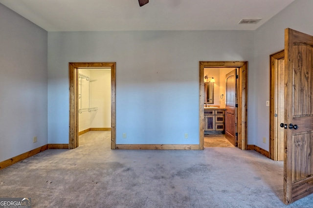 unfurnished bedroom with ceiling fan, a spacious closet, light colored carpet, connected bathroom, and a closet