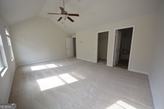 unfurnished bedroom with a closet, a walk in closet, vaulted ceiling, light colored carpet, and ceiling fan