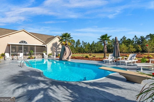 view of swimming pool with a diving board, a water slide, a sunroom, and a patio area