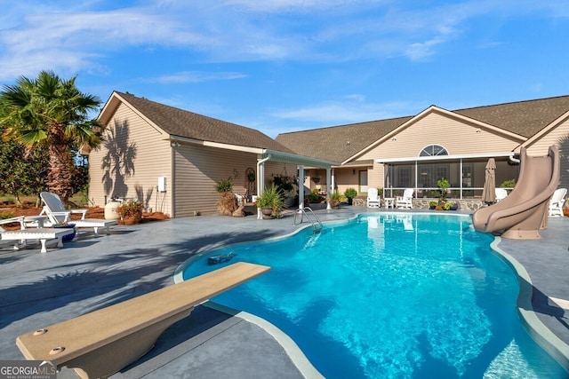 view of swimming pool featuring a diving board, a water slide, a sunroom, and a patio