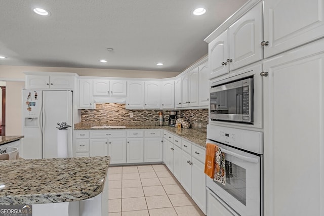 kitchen featuring white appliances, white cabinetry, light tile patterned floors, and stone countertops