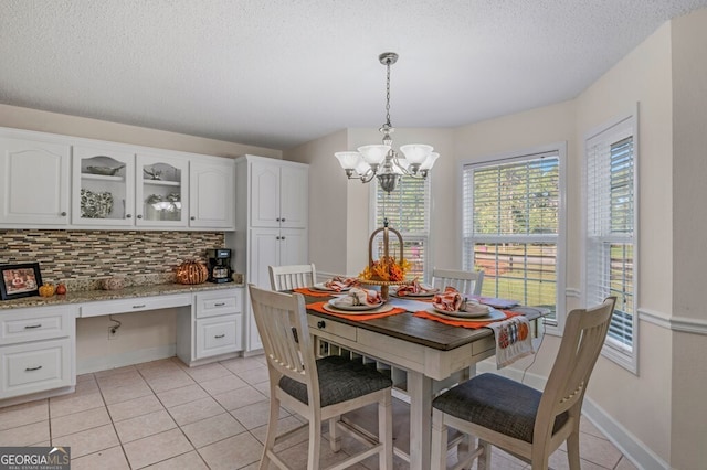 tiled dining space with built in desk, a textured ceiling, and a notable chandelier