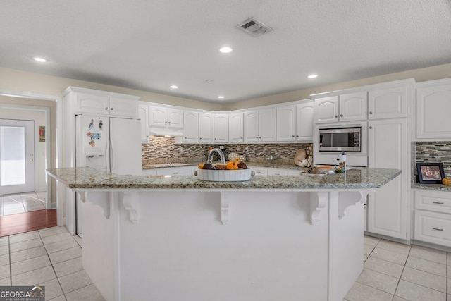 kitchen featuring light stone counters, white cabinetry, a kitchen bar, stainless steel microwave, and a kitchen island with sink