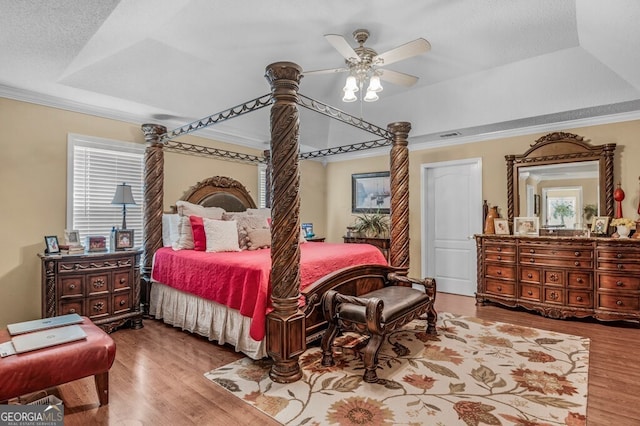 bedroom with hardwood / wood-style flooring, ceiling fan, crown molding, and a tray ceiling