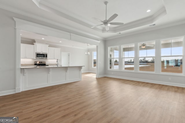 unfurnished living room featuring light hardwood / wood-style flooring, a raised ceiling, ceiling fan with notable chandelier, ornamental molding, and sink