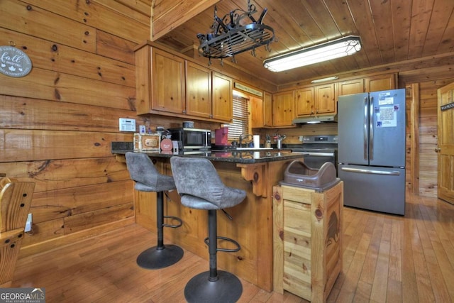 kitchen featuring stainless steel appliances, light hardwood / wood-style floors, a breakfast bar area, a kitchen island, and wooden walls