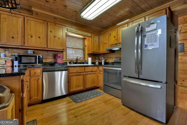 kitchen with stainless steel appliances, wood ceiling, sink, dark stone countertops, and light hardwood / wood-style flooring