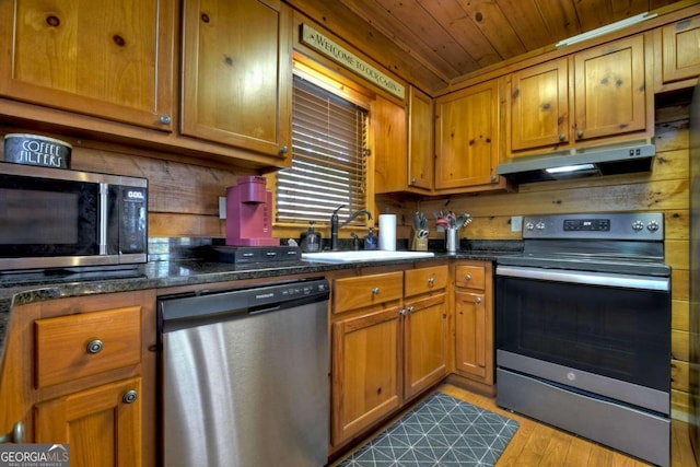 kitchen featuring dark stone counters, appliances with stainless steel finishes, sink, wooden ceiling, and light hardwood / wood-style flooring