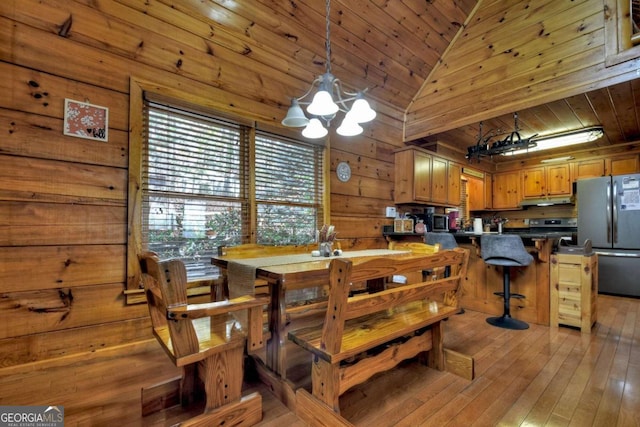 dining room featuring a notable chandelier, high vaulted ceiling, wooden walls, wooden ceiling, and light hardwood / wood-style flooring