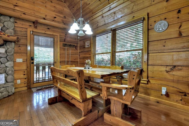 dining room with a wealth of natural light, wood-type flooring, vaulted ceiling, and a notable chandelier