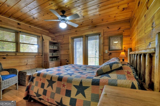 bedroom with hardwood / wood-style floors, ceiling fan, multiple windows, and wooden walls