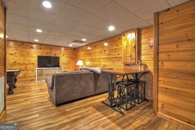 living room featuring light hardwood / wood-style floors, wooden walls, and a paneled ceiling