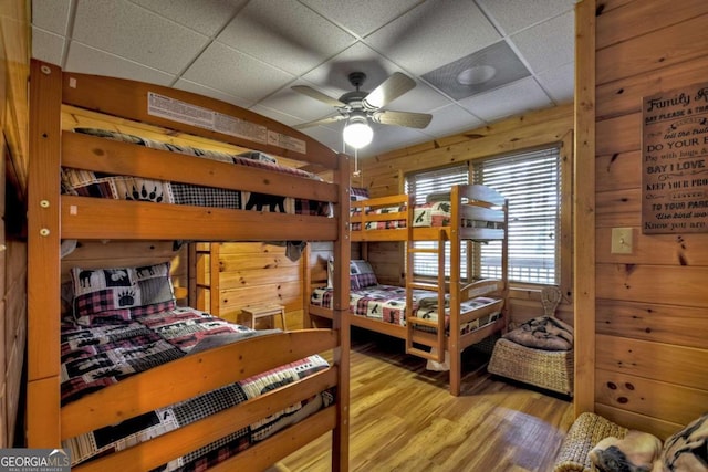 bedroom featuring wood walls, ceiling fan, a drop ceiling, and light hardwood / wood-style floors