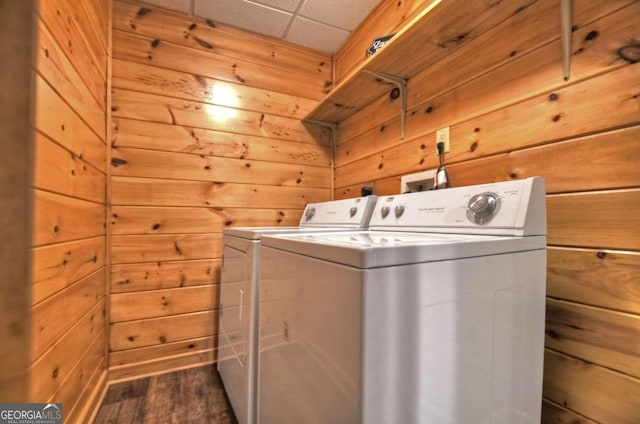 laundry area featuring washing machine and clothes dryer, wooden walls, and dark wood-type flooring