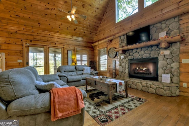 living room featuring high vaulted ceiling, a fireplace, wood walls, and light wood-type flooring