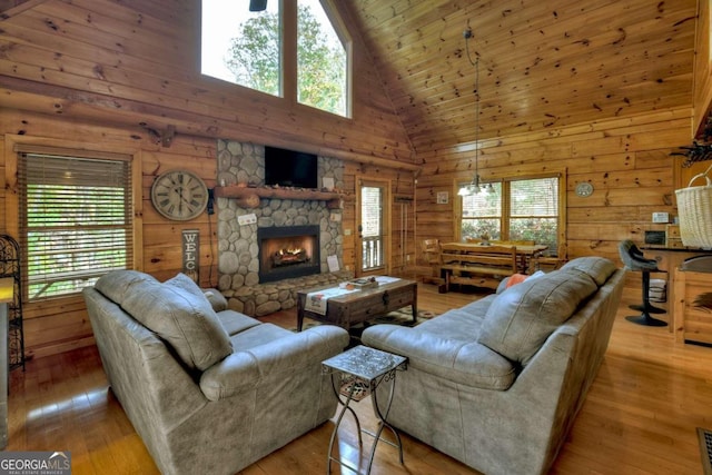 living room featuring high vaulted ceiling, light wood-type flooring, wooden walls, and a healthy amount of sunlight