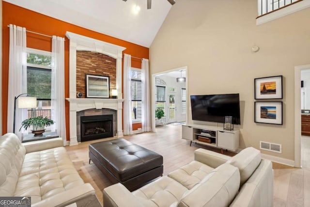 living room with high vaulted ceiling, light hardwood / wood-style flooring, ceiling fan, and a tile fireplace