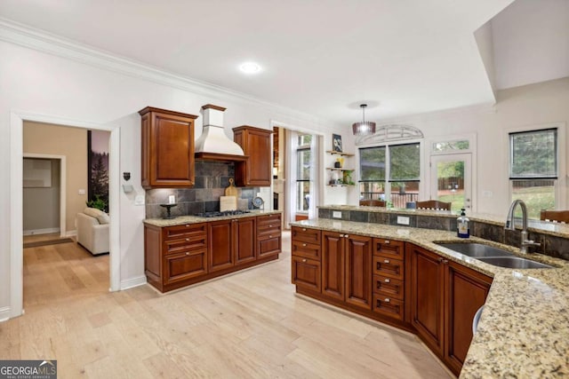 kitchen with premium range hood, light stone countertops, pendant lighting, sink, and light hardwood / wood-style floors