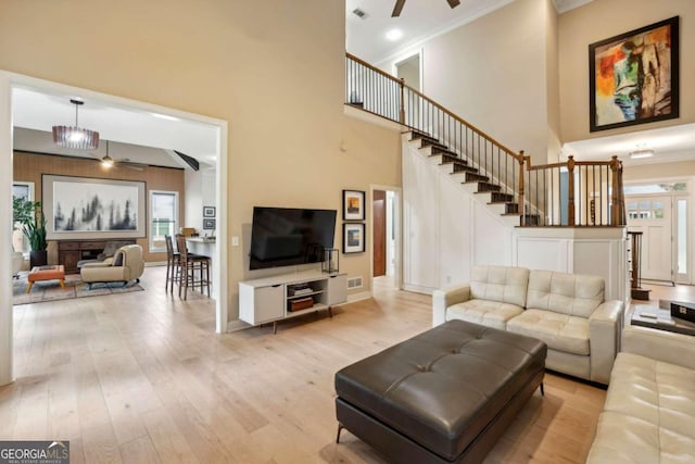 living room with a high ceiling, ceiling fan with notable chandelier, light wood-type flooring, and crown molding