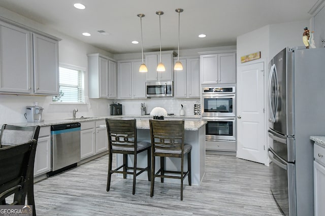 kitchen with stainless steel appliances, light hardwood / wood-style floors, light stone counters, a kitchen island, and pendant lighting