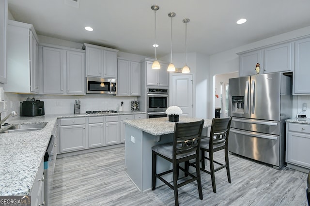 kitchen featuring light wood-type flooring, appliances with stainless steel finishes, a kitchen bar, hanging light fixtures, and sink