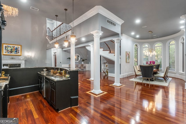 kitchen with dark wood-type flooring, kitchen peninsula, crown molding, stone countertops, and pendant lighting