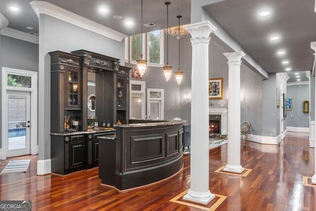 bar featuring light stone counters, ornamental molding, decorative light fixtures, ornate columns, and dark hardwood / wood-style floors