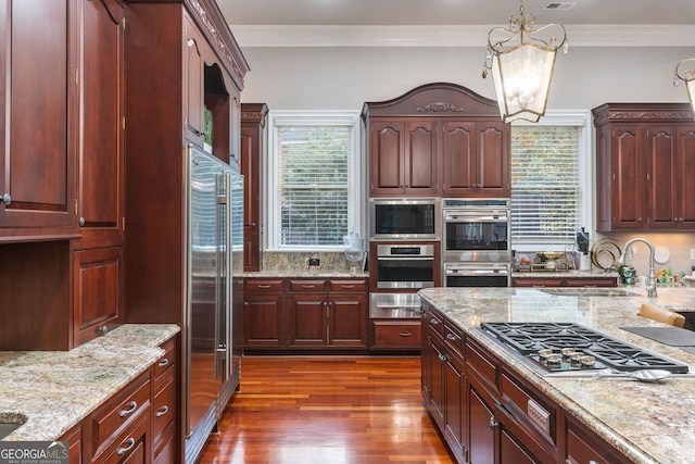 kitchen with light stone counters, stainless steel appliances, a notable chandelier, hanging light fixtures, and dark wood-type flooring