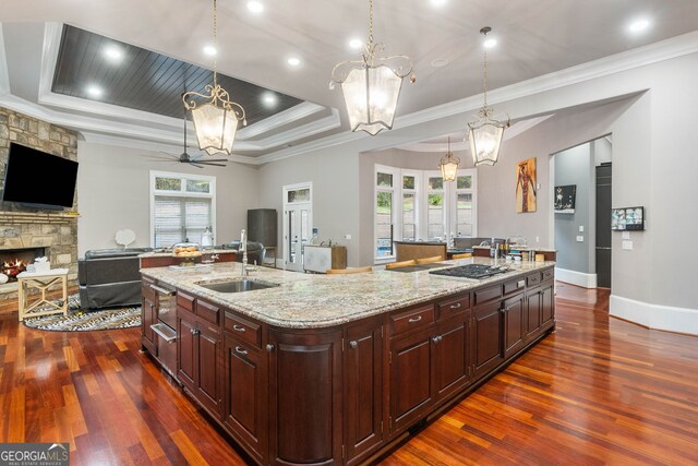 kitchen featuring a fireplace, dark hardwood / wood-style floors, light stone countertops, sink, and a spacious island