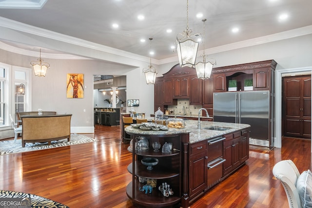 kitchen featuring a kitchen island with sink, ornamental molding, dark hardwood / wood-style floors, high end refrigerator, and pendant lighting