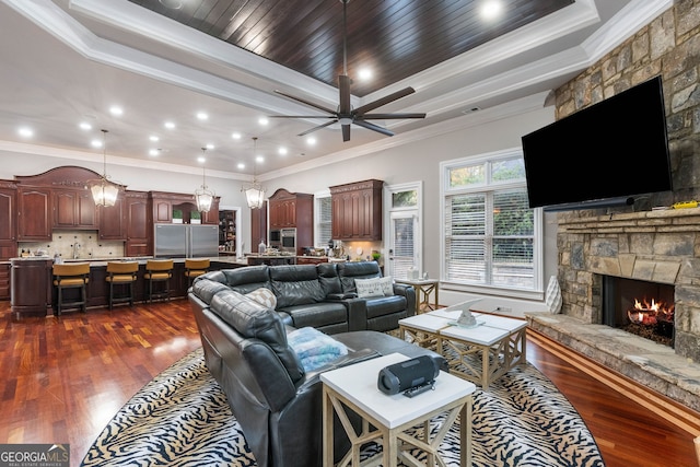 living room with ceiling fan, dark hardwood / wood-style floors, a stone fireplace, and crown molding