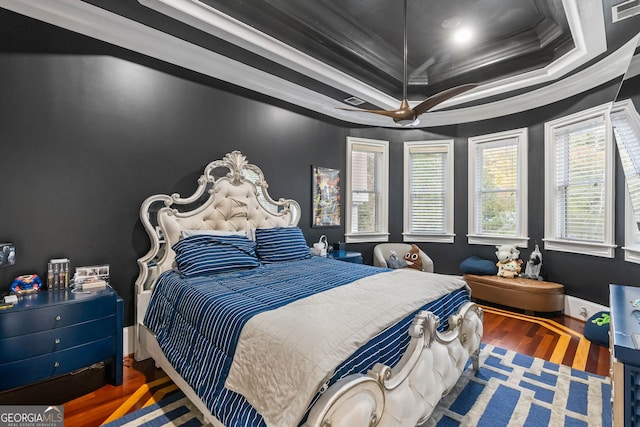 bedroom with ceiling fan, a tray ceiling, wood-type flooring, and ornamental molding