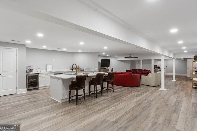 kitchen featuring wine cooler, white cabinetry, light hardwood / wood-style floors, and a kitchen breakfast bar