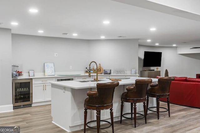 interior space with beverage cooler, white cabinets, sink, an island with sink, and a kitchen breakfast bar