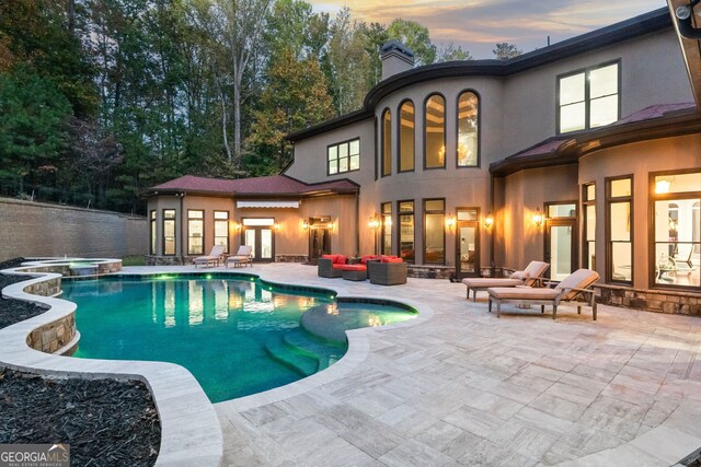 pool at dusk with a patio, an in ground hot tub, and an outdoor living space