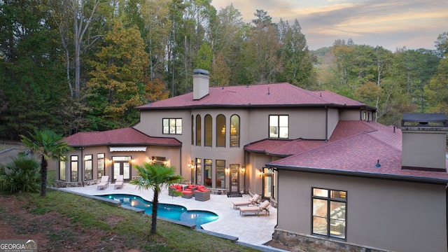 back house at dusk with outdoor lounge area and a patio area