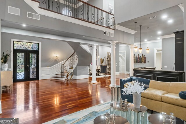 living room with hardwood / wood-style flooring, ornamental molding, a towering ceiling, decorative columns, and french doors