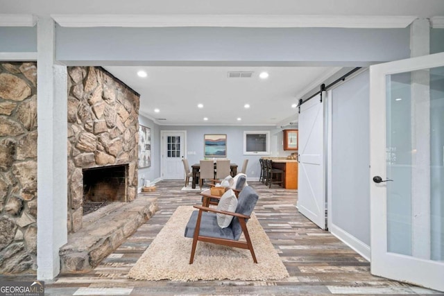 living room featuring hardwood / wood-style flooring, a fireplace, ornamental molding, and a barn door