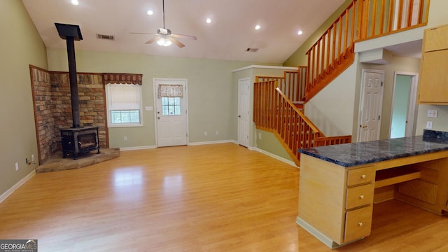 kitchen featuring light hardwood / wood-style floors, kitchen peninsula, ceiling fan, a wood stove, and lofted ceiling