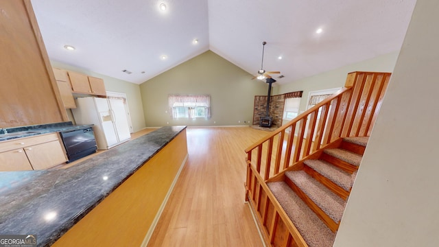 kitchen with light brown cabinetry, high vaulted ceiling, a wood stove, light wood-type flooring, and dishwasher