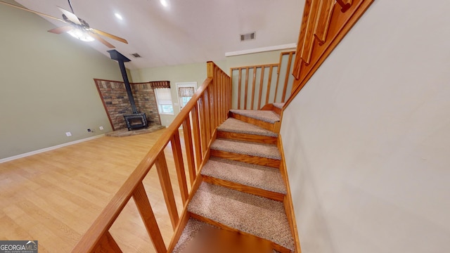 staircase with hardwood / wood-style floors, a wood stove, vaulted ceiling, and ceiling fan